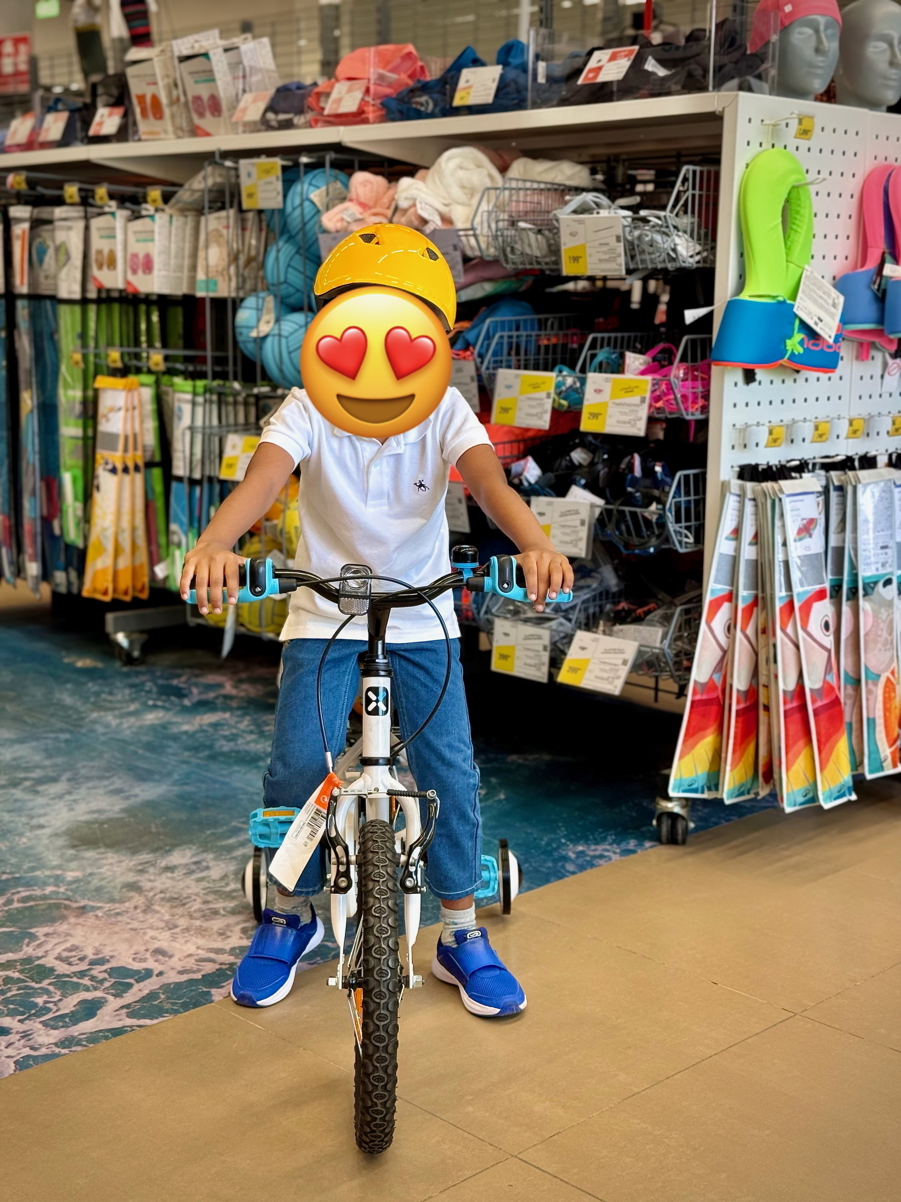 A child wearing a yellow helmet is sitting on a small white bicycle with training wheels inside a store.