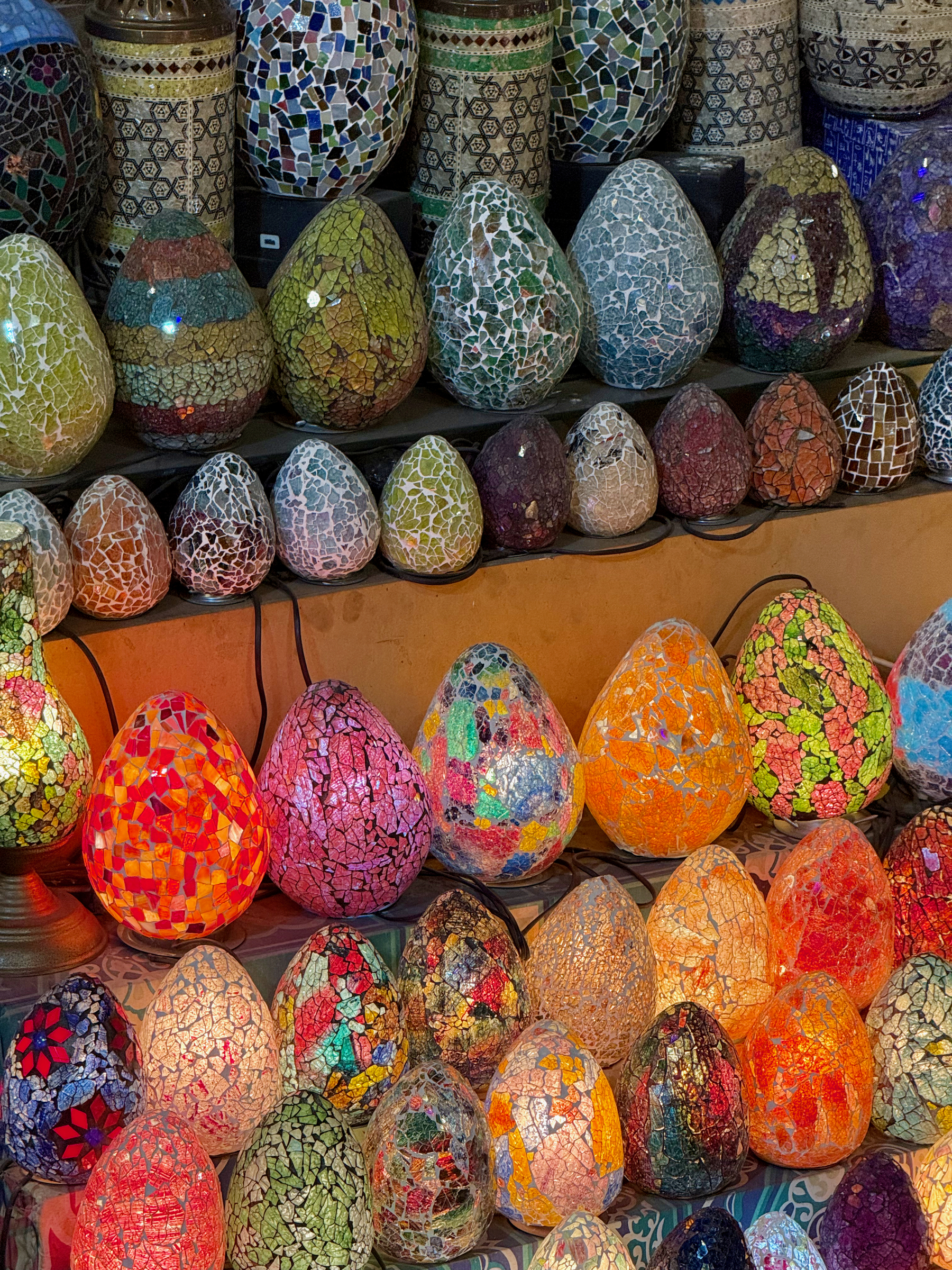 A collection of colorful mosaic lamps in various shapes and sizes is displayed, illuminated to highlight their intricate designs.