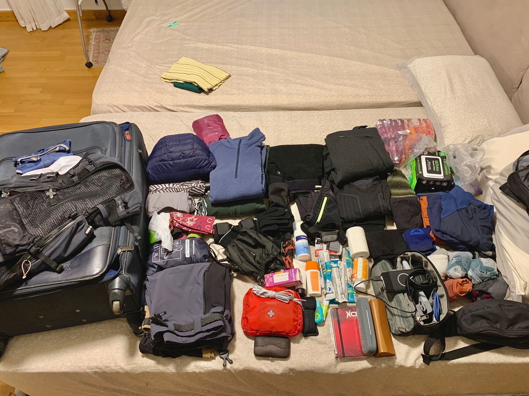 Auto-generated description: A bed is covered with an assortment of neatly arranged travel items, including clothes, toiletries, and other accessories, alongside a suitcase.