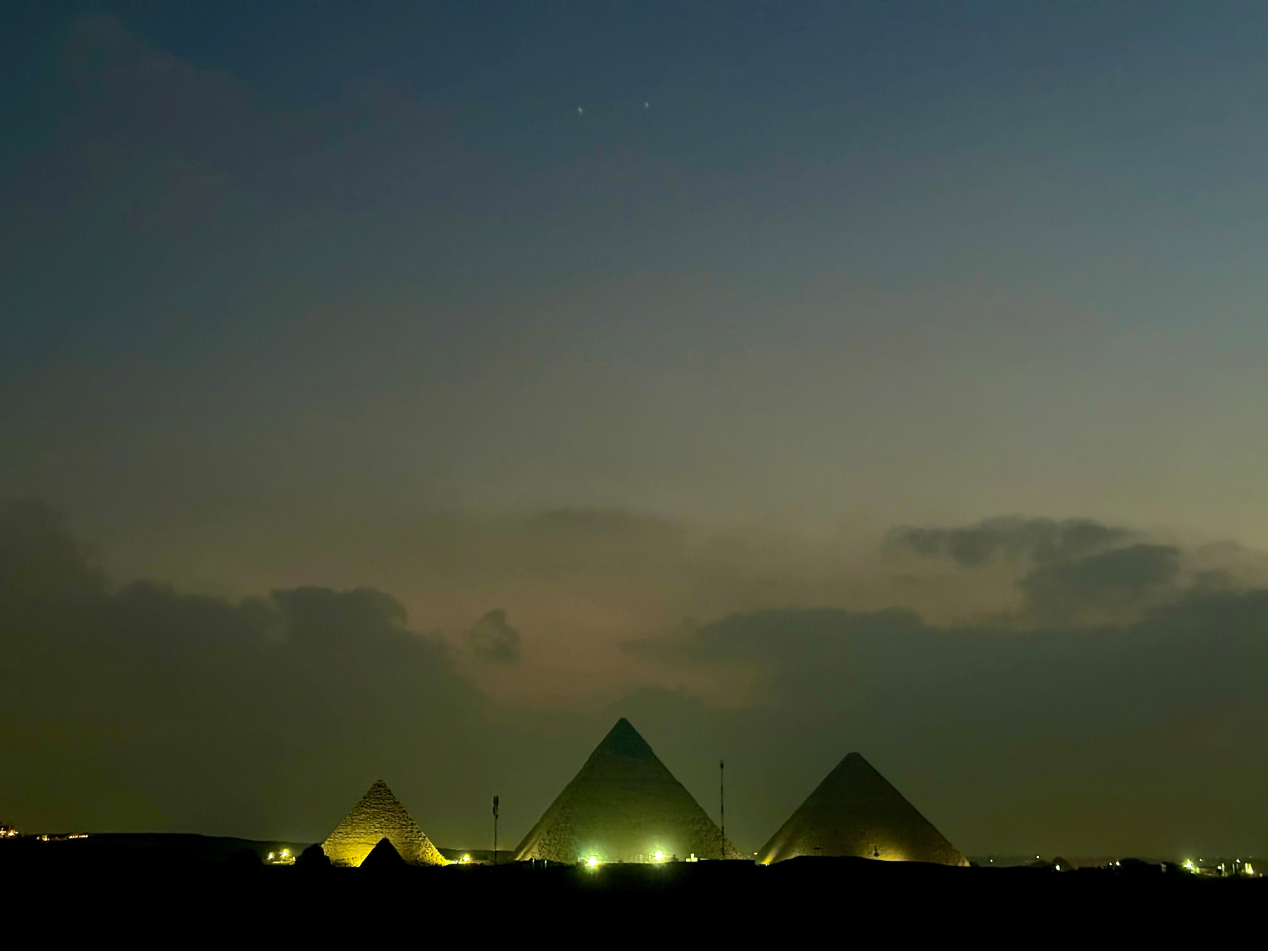 The illuminated pyramids stand against a darkening sky just before sunrise.