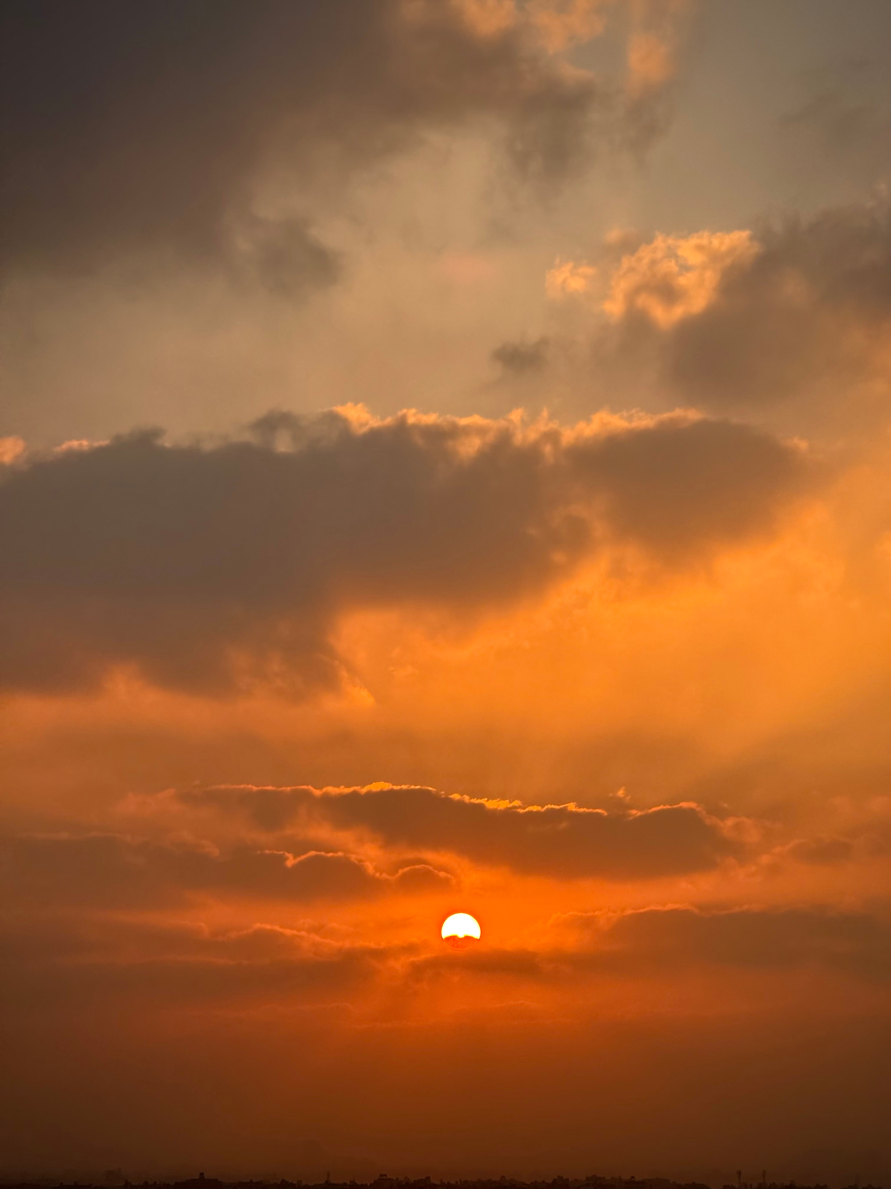 Auto-generated description: A vibrant sunrise is seen with the sun partially obscured by clouds, casting an orange and golden hue across the sky.