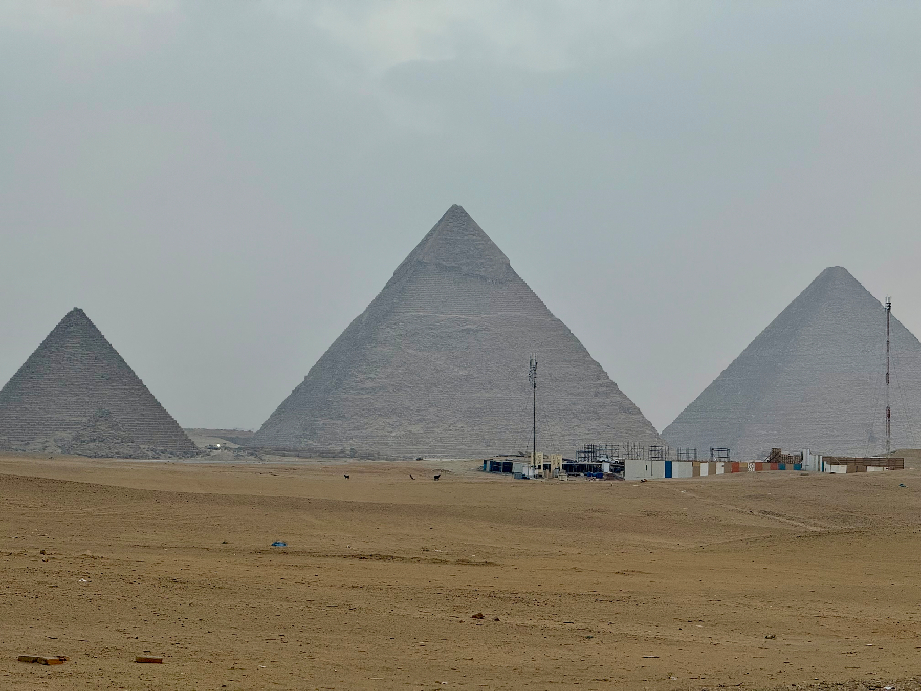 Three large pyramids stand on a sandy desert landscape under a cloudy sky.