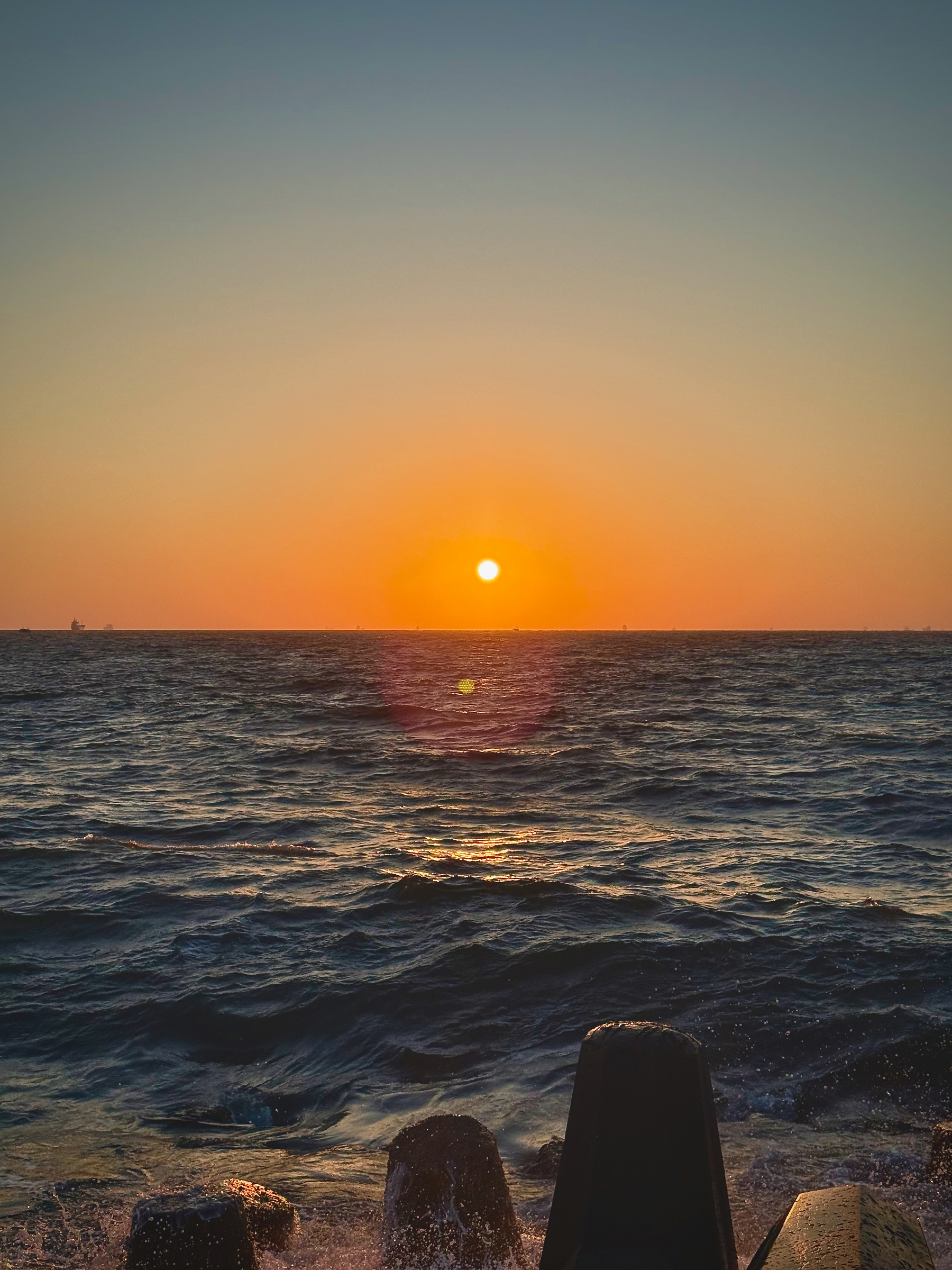 Auto-generated description: A vibrant sunset casts a warm orange glow over the rippling ocean waves and concrete coastal barriers.